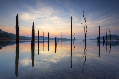 Wooden posts in lake against sky during sunset