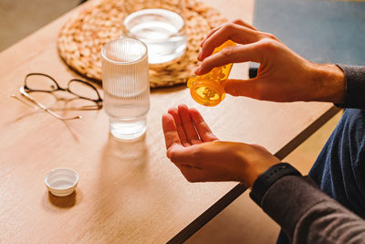 Unrecognizable man pouring tablets from orange plastic bottle into his hand