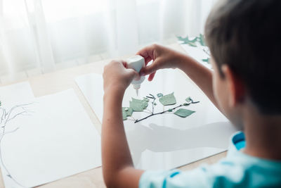 Close up of child sitting by desk and making picture from dry birch leaves. autumn activities 