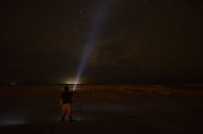 Rear view of man with illuminated flashlight standing against star field at night