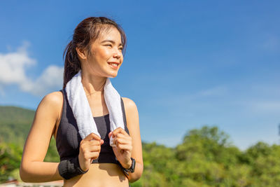 Smiling young woman using smart phone against sky