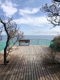 Wooden bench on pier by sea against sky