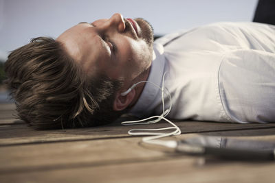 Businessman listening music through mobile phone while lying on boardwalk