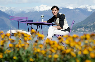 Portrait of smiling mature woman sitting on chair against lake