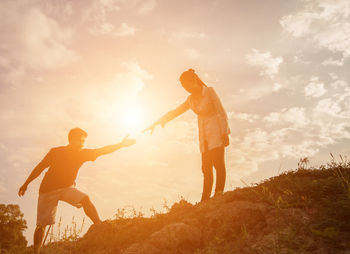 Low angle view of people with arms raised against sky during sunset