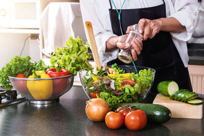 Midsection of man seasoning salad in kitchen