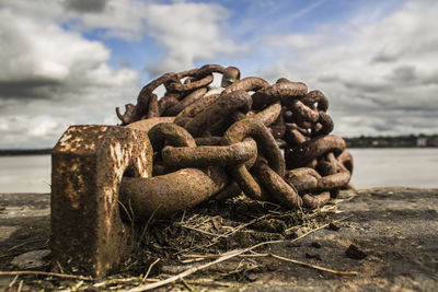 Close-up of rusty chain tied up on beach against sky