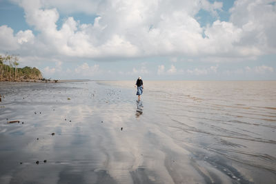 Rear view of woman walking at beach against sky