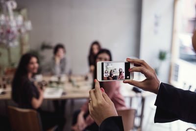 Cropped hands of woman photographing female colleagues sitting at table in perfume workshop