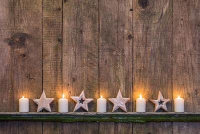 Illuminated candles with star shape decorations on wooden fence during christmas