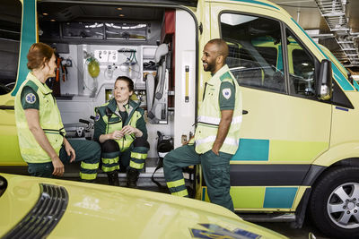 Male and female paramedics talking while sitting in ambulance at parking lot