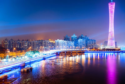 Illuminated buildings by river against sky at night