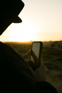 Hand holding smart phone against sky during sunset