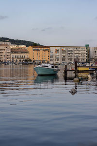 Sailboats moored on sea by buildings in city against sky