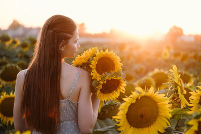 Woman on sunflower field young cheerful person holding hands up in air and looking at sunrise