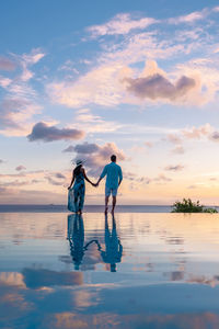 Rear view of woman standing at beach against sky during sunset