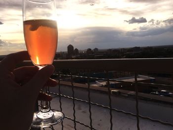 Close-up of hand holding drink against sunset