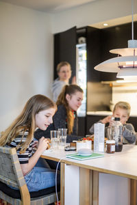 Girl talking to smart speaker while sitting with family at table in modern home