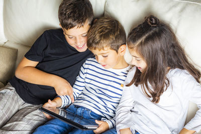 High angle view of siblings using digital tablet while sitting on sofa at home