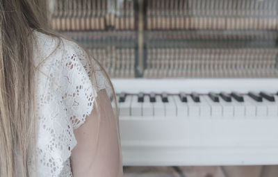 Cropped image of woman sitting by grand piano at home