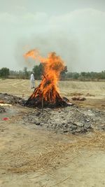 Man standing by bonfire on land against sky