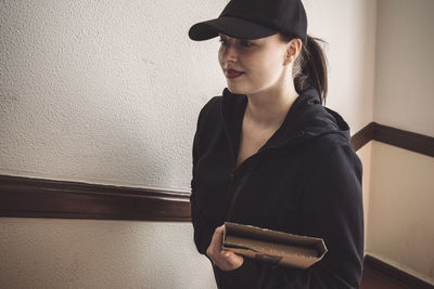 Confident delivery woman with package against wall