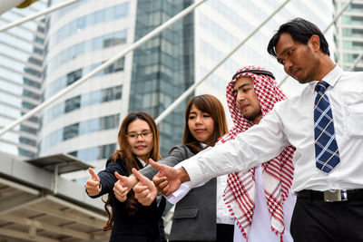 Low angle view of colleagues showing thumbs up against skyscraper in city