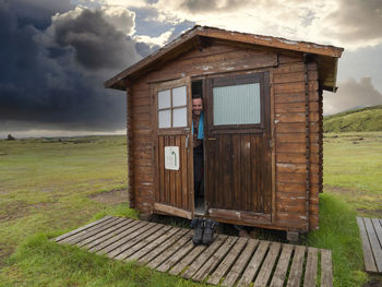 Smiling male tourist peeking from wooden cottage door