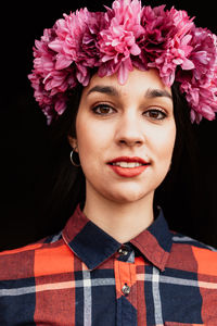 Portrait of woman wearing flower standing against black background