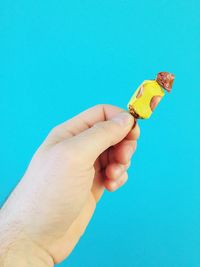 Cropped hand holding chocolate against blue background