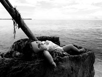 Doll lying in sea against sky