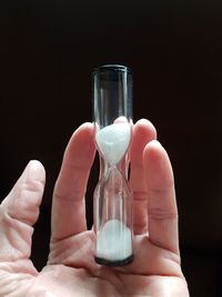 Close-up of hand holding hourglass against white background