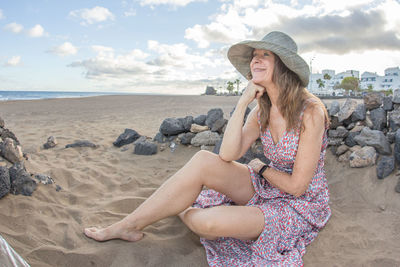 Young woman sitting at beach against sky