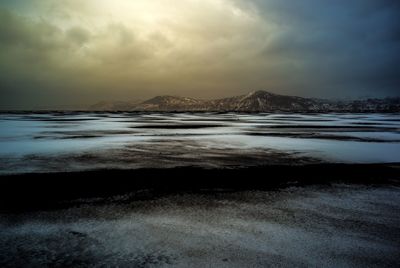 Snow covered landscape against cloudy sky