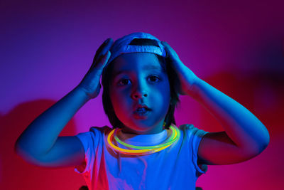 Cyberpunk boy child in white t shirt and sunglasses neon sticks on neck listening music on wall