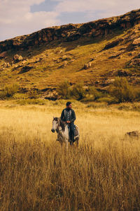 Man sitting on field against sky