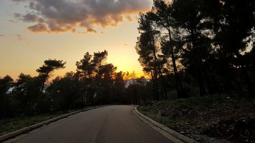 Road amidst trees against sky during sunset