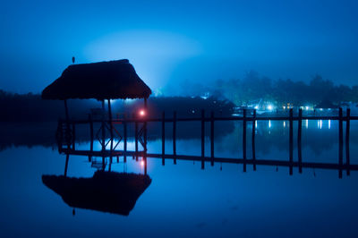 Silhouette swimming pool by lake against sky at night