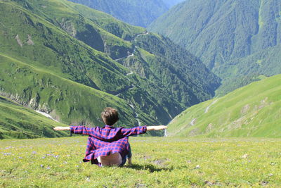 Rear view of man sitting on landscape against mountains