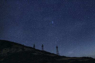 Electricity pylons on hill against starry sky