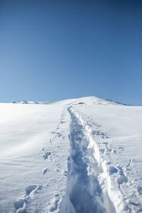 Snow covered landscape against clear blue sky