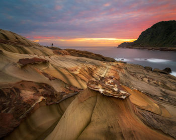 Rocks at sea shore against sky during sunset