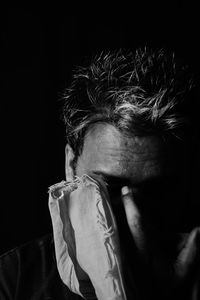 Close-up of man covering face against black background