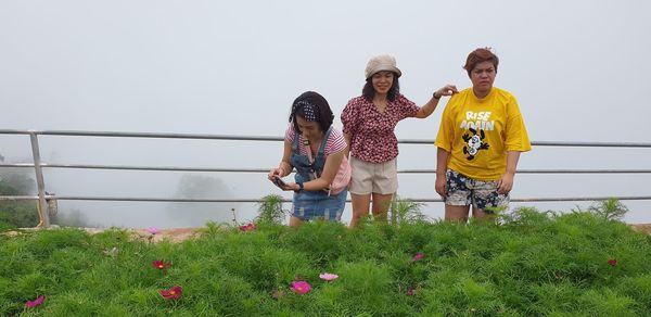 People standing by flowering plants against sky