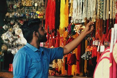 Side view of young man standing by multi colored necklace for sale at market stall