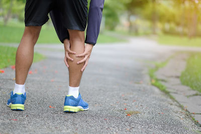 Low section of man touching calf while standing on footpath