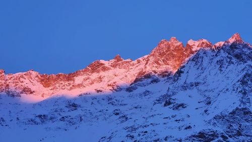 Low angle view of snowcapped mountains against clear blue sky