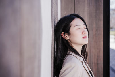 Relaxed beautiful chinese business woman standing over wood signs background with eyes closed