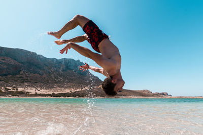 Side view of man jumping in sea against clear sky