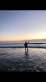Silhouette man in sea against sky during sunset
